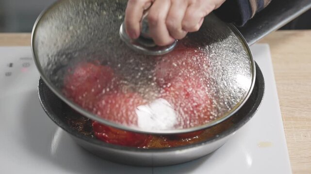 lid is placed over tomatoes and garlic cooking in oil in hot pan collecting condensation on the stove in home kitchen to prepare healthy Italian tomato sauce meal; food closeup