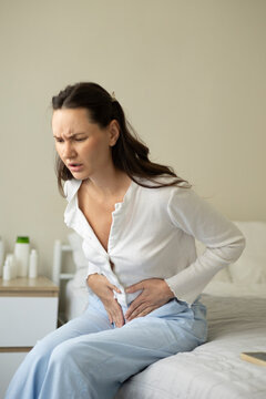 Woman suffering from menstrual pain and abdominal cramps while sitting on a bed at home