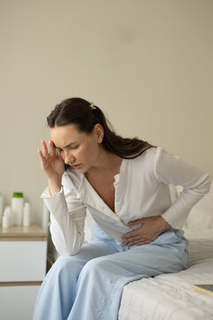 Woman suffering from menstrual pain and abdominal cramps while sitting on a bed at home