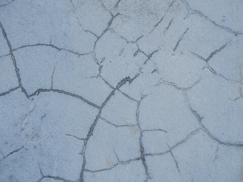 cracked grey concrete surface showing detailed fracture lines and weathered texture. Ideal as a background or texture overlay for graphic design, web layouts, construction concepts, and architectural