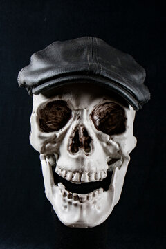 Skeleton skull wearing black flat cap on dark background