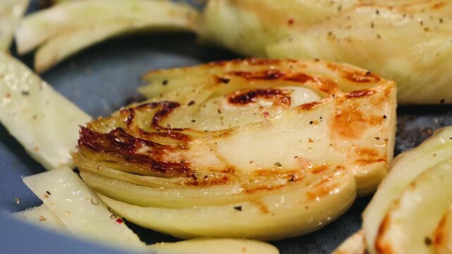Close-up of fennel wedges frying in pan with spices. Grilled fennel slices, healthy vegetable cooking process.