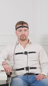 Anxious man sitting on a chair with sensors on his body undergoes a polygraph examination, responding to questions during an interrogation while connected to a lie detector machine