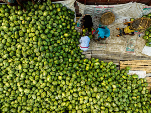 Aerial view of Sadarghat with workers sorting a large pile of fresh watermelons on a wooden boat deck in Dhaka, Dhaka Division, Bangladesh.