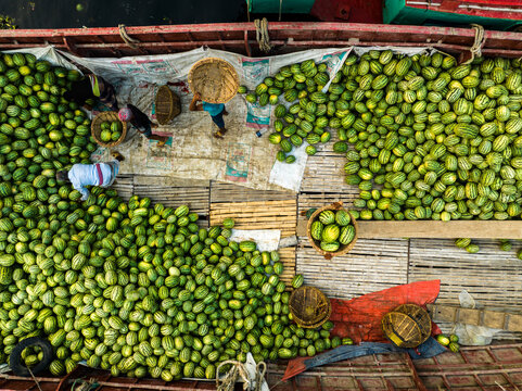Aerial view of workers loading and unloading large quantities of watermelons onto a wooden boat at Sadarghat in Dhaka, Dhaka Division, Bangladesh.