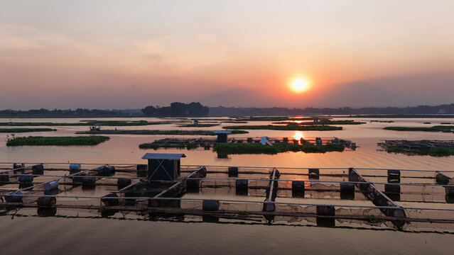 Aerial view of Cengklik Reservoir at sunset with fish farming cages and Mount Merapi and Mount Merbabu in the background in Ngemplak, Central Java, Indonesia.