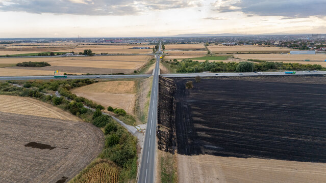 Aerial view of a rural road intersection surrounded by agricultural fields, including a section of scorched earth, under a cloudy sky in Sremska Mitrovica, Vojvodina, Serbia.