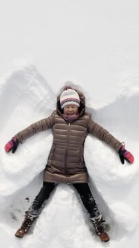 Asian woman playing in the snow and making snow angels. Vertical Video.