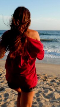Attractive and playful woman running along the beach. Vertical video.