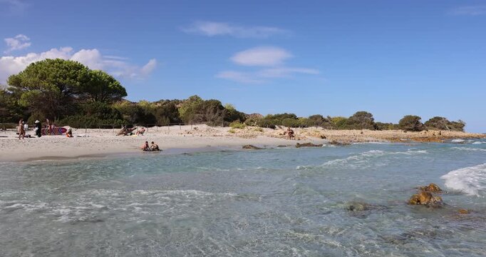 Vista della spiaggia dell'Oasi Biderosa, a Orosei (Sardegna, Italia), con persone che si rilassano sulla sabbia bianca e acque turchesi e cristalline.