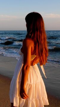 Beautiful woman in a white dress at the beach at sunset. Vertical video.