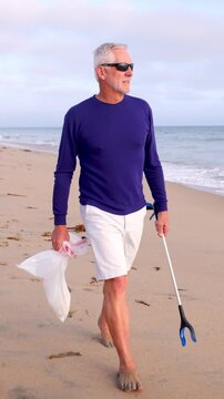 Mature 66 year old man picking up trash from a beach in Southern California. Vertical Video.