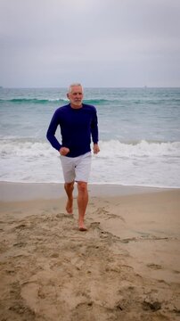 A mature 66 year old man jogging at the beach in Southern California. Slow Motion. Vertical Video.