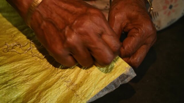 An elderly woman sews a rice sack by hand with thread and needle. Heavy-duty needles and thick plastic thread are commonly used tools for sealing bulk transport sacks. Wholesale markets (mandis)