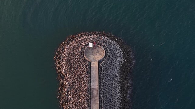 An aerial view showing a circular breakwater complete with a small lighthouse and tetrapods extending toward the deep blue sea highlights the geometry and texture of the coastline
