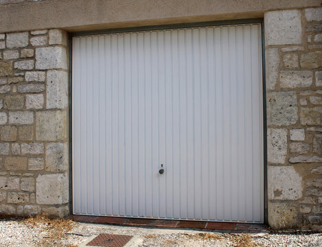 Porte de garage basculante blanche install&eacute;e dans une fa&ccedil;ade en pierre de taille traditionnelle
