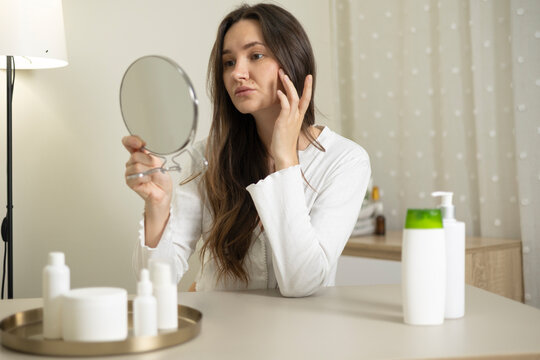 Woman examining her face in a mirror during a daily skincare and self-care routine at home
