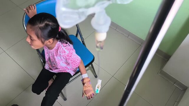 a little girl sitting on a chair with a tube and IV pole attached to her right hand