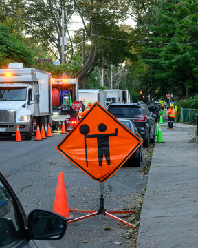 Traffic control flagger sign with utility trucks and road crew on a residential street at dawn in Toronto, Ontario, Canada