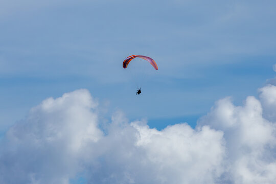 Aerial view of a paragliding tandem soaring through the blue sky with fluffy white clouds in Slovenia.