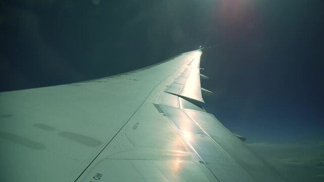 View of a commercial airplane wing flying high above the clouds in the blue sky. Bright sunlight and reflections shining on the aircraft metal surface, beautiful sun flare during the flight.