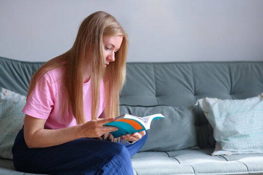 Woman relaxing on a sofa with paper books, promoting reading as mindful leisure, digital detox and stress relief.
