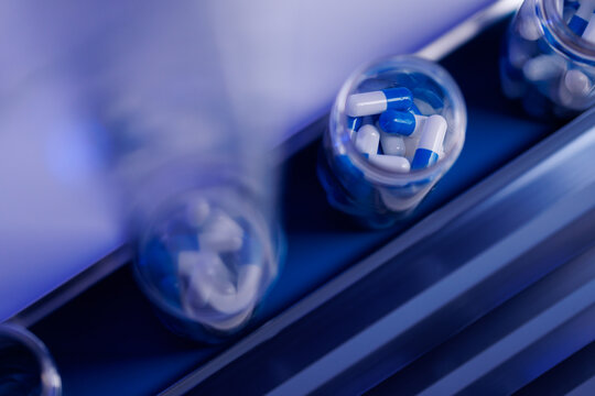 Macro view of blue and white capsule pills in glass vials moving on conveyor for pharmaceutical packaging background, top view