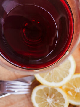 Red wine in a glass on a wooden table, top view, surrounded by fresh lemon slices and a fork, preparing for a gourmet dining experience or traditional asado meal