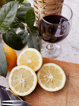 Still life composition with red wine glass, lemons, and bay leaves on a rustic wooden cutting board, preparing ingredients for a gourmet outdoor barbecue or traditional Asado