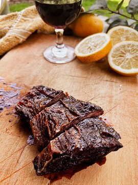 Sliced grilled beef short ribs resting on a wooden cutting board, serving alongside a glass of red wine and fresh lemon halves, creating an inviting Argentine asado meal
