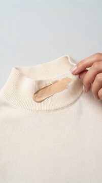 Liquid foundation makeup stain on white knitted sweater collar close up