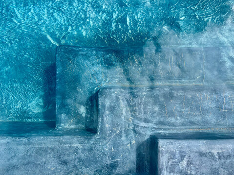 Overhead underwater view of weathered concrete steps with rippling turquoise water and light patterns