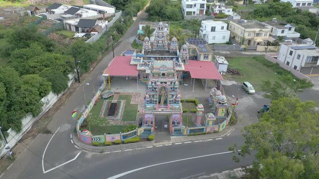 Aerial view of the colorful Hindu temple in Cap Malheureux surrounded by lush greenery and residential buildings in Ile, Riviere du Rempart, Mauritius.