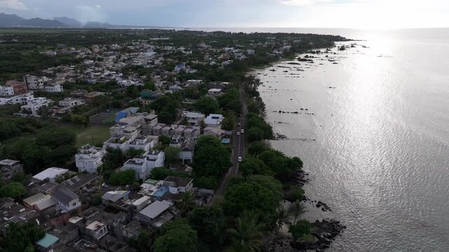 Aerial view of Trou aux Biches Beach coastline with residential buildings, lush trees, and a coastal road along the Indian Ocean in Pamplemousses District, Mauritius.