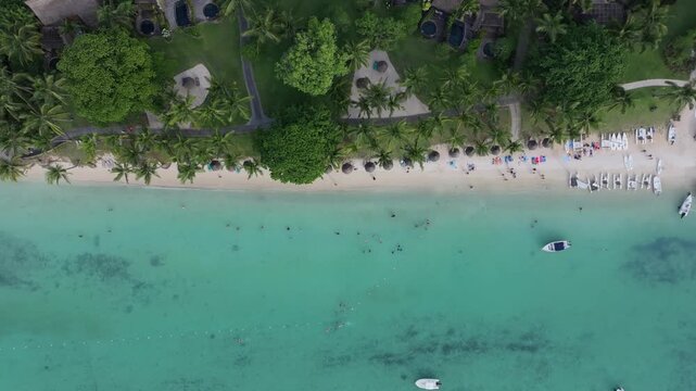 Aerial view of Trou aux Biches Beach with turquoise water, white sand, palm trees, and a small boat in Pamplemousses District, Mauritius.