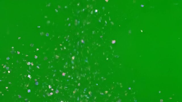 Iridescent microplastic shimmer flakes floating against a solid green screen background