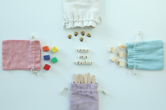 Arts and crafts message surrounded by wooden blocks, craft sticks, beads and pastel fabric bags in a creative flat lay.