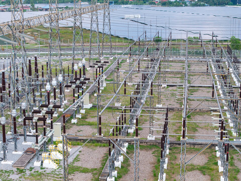 Aerial view of a high-voltage transmission substation with complex electrical infrastructure and a large solar panel farm in the background in Central Seberang Perai, Penang, Malaysia.