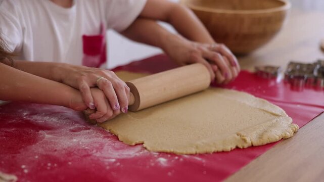Close up detail of mother and daughter rolling out cookie dough using rolling pin while making Christmas cookies