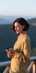 Obraz premium Young woman on mountain balcony using smartphone and holding drink for lifestyle background and travel banner