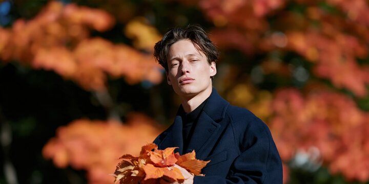Autumn male portrait holding orange leaves for seasonal banner and fall background design with moody fashion styling