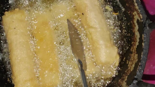 Spring rolls deep frying in hot bubbling oil in a metal pan for commercial food preparation