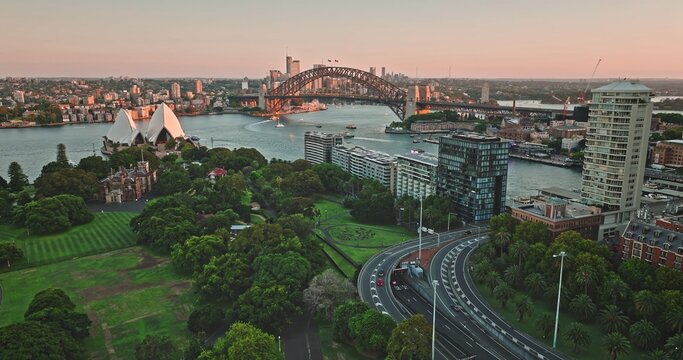 Aerial view of Sydney Opera House and Sydney Harbour Bridge with lush parkland, modern buildings, and city traffic in Sydney, New South Wales, Australia.