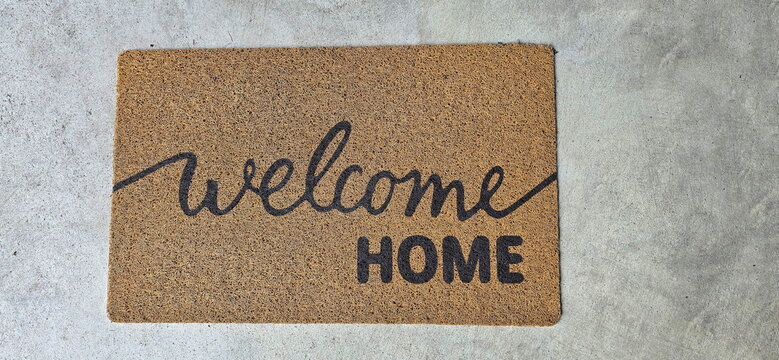 A light brown natural coir doormat printed with the black text "welcome HOME." The mat is placed on a concrete floor. Coconut Doormat for Indoor Use - Dirt Trapper Mat Natural, Coconut Mat Welcome
