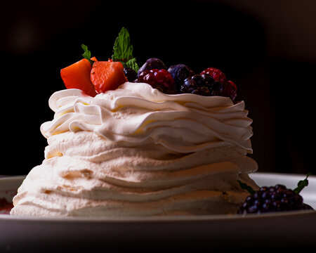 Mini pavlova de merengue con crema batida frutillas ar&aacute;ndanos y moras sobre fondo negro &aacute;ngulo bajo