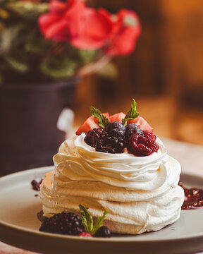 Mini pavlova de merengue con crema batida frutos rojos frutillas moras y coulis en plato &aacute;ngulo bajo