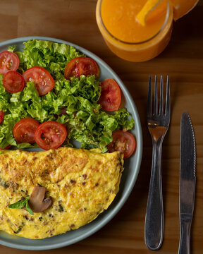Omelet de huevos y hongos con ensalada de lechuga tomate y jugo de naranja en mesa de madera vista cenital