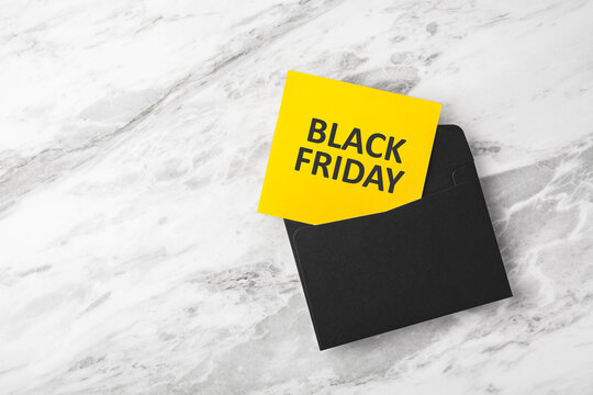 Black friday background, yellow card with black friday text in envelope on marble background, copy space