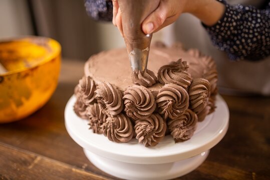 Hand piping chocolate buttercream rosettes on round layer cake in cozy kitchen setting