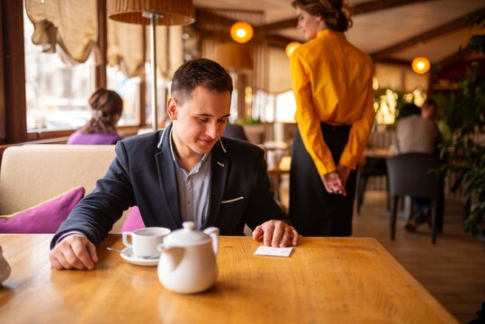 Happy young man looking at the napkin on the table young woman left